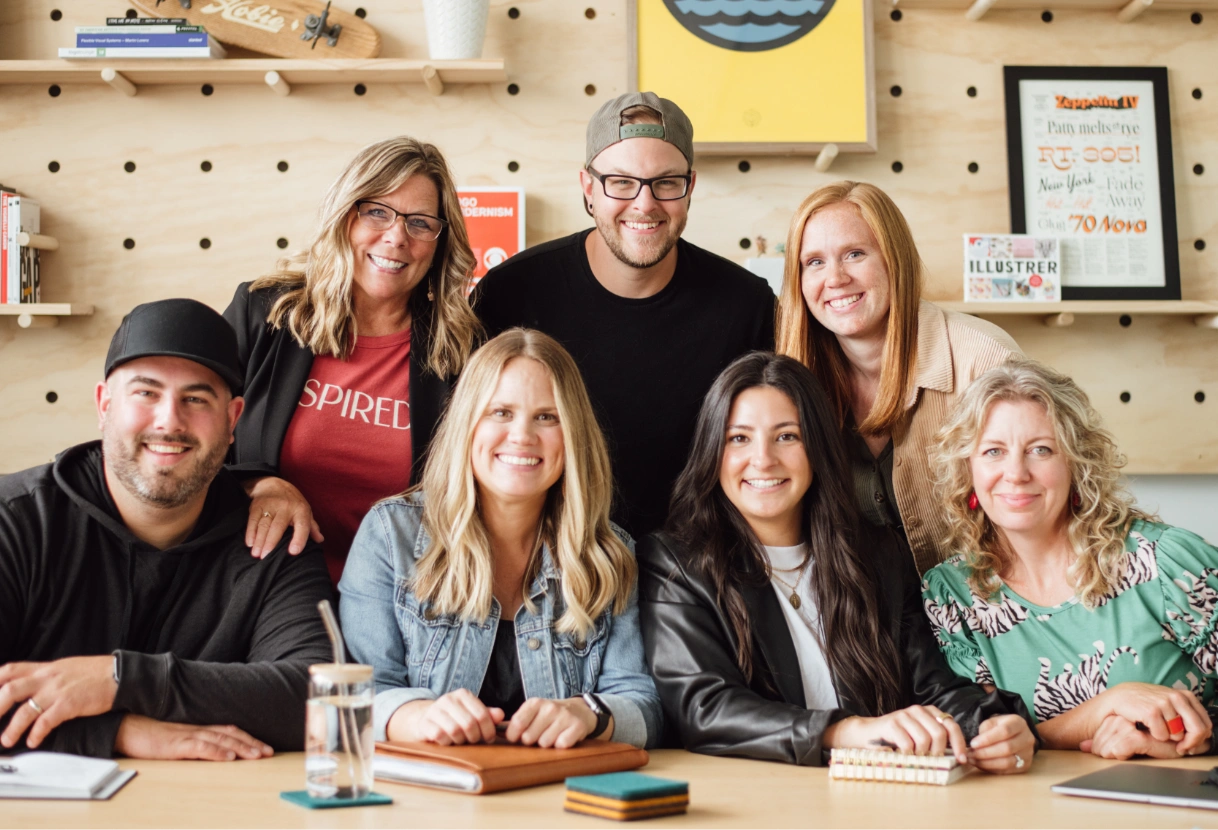 7 team members grouped at a desk, looking at the camera.